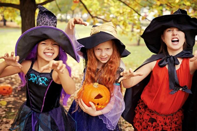 Kids in halloween costume in a park with fall leaves on trees